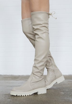 Beżowe kozaki za kolano z gładkiej skóry, z okrągłym noskiem, masywną białą podeszwą oraz dopasowanym sznurowaniem na górze. Zapięcie na suwak z boku.