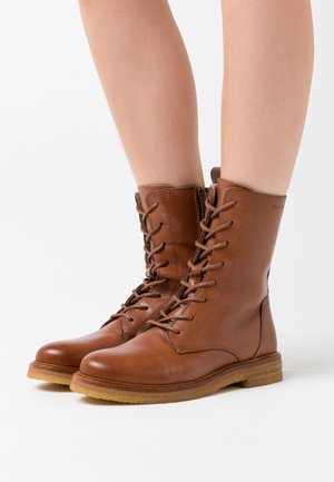 Stivali marroni in pelle con lacci e cerniera laterale, caratterizzati da punta tonda, suola robusta e dettagli con cuciture a contrasto.
