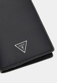 Portefeuille noir texturé avec un plaque logo argenté en forme de triangle. Le design est compact avec des coutures visibles le long des bords.