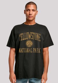 Black cotton t-shirt featuring a vintage-style yellow print stating "YELLOWSTONE NATIONAL PARK" with a graphic logo centered below.