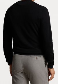 Pull noir en maille avec encolure ronde et manches longues, assorti à un pantalon gris clair doté d'une poche arrière et d'un détail bouton.