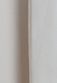 Tissu beige clair avec un motif texturé en ribbes. Les bords sont finis avec des coutures nettes, mettant en valeur un aspect doux et tissé.