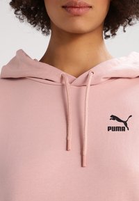 Ljusrosa hoodie med dragkedja och en svart Puma-logotyp, med snörning och en mjuk, strukturerad tyg. Perfekt för avslappnad komfort.