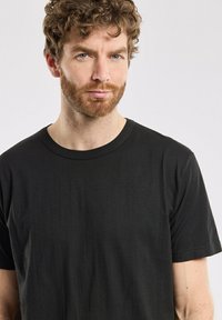 T-shirt en coton noir avec un col rond et des manches courtes. Texture lisse, design simple, sans motifs ni accents visibles.