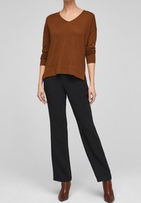 Brun stickad tröja med v-ringning, långa ärmar och sidospalter, matchad med svarta vida byxor och bruna ankelskor.