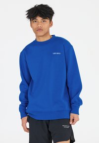 Blauwe sweatshirt met ronde hals, lange mouwen en ribgebreide manchetten. Bevat de tekst "LES'ARCS" in het wit op de borst. Het materiaal lijkt zacht en textuur te hebben.