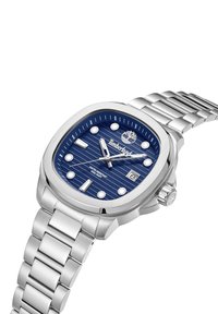 Orologio in acciaio inossidabile con un quadrante blu testurizzato, indicatori delle ore argentati e display della data. Presenta un bracciale metallico collegato e una corona.