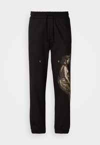 Black sweatpants feature an elastic waistband with drawstrings. One side displays a large, textured graphic in earthy tones depicting a figure.