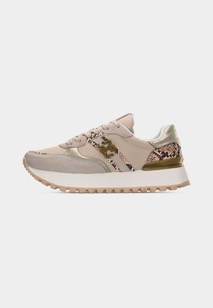 Zapatilla beige con suela texturizada, detalles con estampado de serpiente, detalles metálicos, cordones delanteros y emblema con logo en el costado, mostrada en vista lateral.