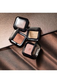 Fyra öppna KIKO-ögonskuggor i brons-, guld-, rosa- och rosfärgade nyanser arrangerade på bronsfärgat texturerat tyg.