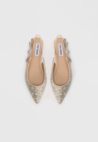 Μπεζ στιλόθοι με αιχμηρή μύτη και κεντημένα σπινθιρίζοντα κρύσταλλα, καθώς και πλαϊνές κορδέλες, της μάρκας Steve Madden, απεικονιζόμενα από πάνω σε λευκό φόντο.