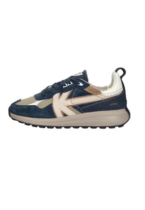 Sneaker in marineblauw en beige met witte accenten, een dikke zool, veters en een lusje aan de achterkant, gezien vanaf de buitenkant.