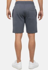 Grijze sportshorts met een trekkoord in de taille, zijzakken en een achterzak. De stof is soepel met een relaxte pasvorm. Gdragend met witte sneakers.