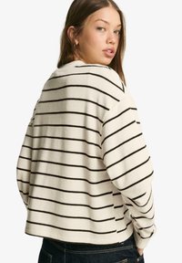 Csíkos pulóver krém színben fekete vízszintes csíkokkal, laza szabással, lekerekített nyakkivágással és puha textúrával. Hátulnézet.