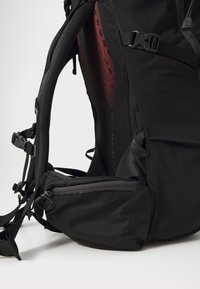 Svart nylon ryggsekk med mesh polstring, justerbare stropper, glidelåslommer og et elegant design med røde detaljer.
