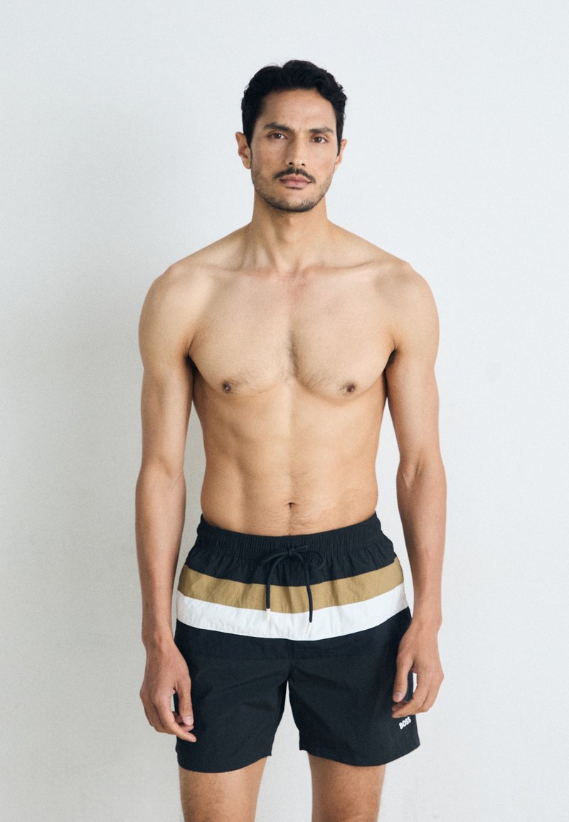 Schwarze Schwimmshorts mit horizontalen Streifen in Weiß und Khaki, aus leichtem Material gefertigt, mit elastischem Bund und Kordelzug.