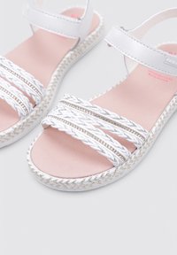 Sandalias blancas con tiras trenzadas y acentos brillantes. Plantilla rosa suave y suela blanca texturizada con patrón de espiga.