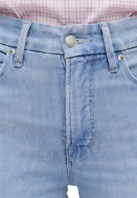 Ανοιχτό μπλε τζιν με κούμπωμα με κουμπιά και θηλιές για ζώνη, φορεμένα με ροζ και λευκό καρό πουκάμισο.