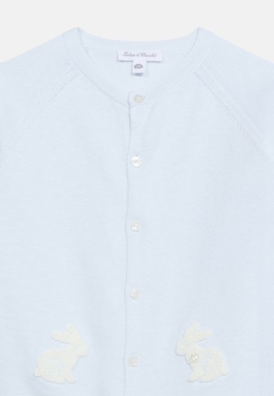 Ανοιχτό γαλάζιο μπουφάν μωρού με στρογγυλή λαιμόκοψη, κουμπιά μπροστά και δύο λευκές εφαρμογές λαγουδάκι κοντά στο κάτω μέρος.