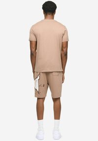 Bež pamučna majica i odgovarajuće kratke hlače, s bijelim logotipom i uzorkom prskanja, kratkih rukava i bočnih džepova.