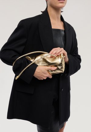 Bolso metálico dorado con textura suave, de forma estructurada y correa delgada. Sostenido contra un blazer negro.