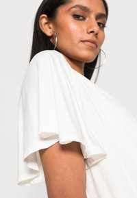 Weißes T-Shirt mit kurzen, ausgestellten Ärmeln. Aus weichem Stoff gefertigt, mit lockerer Passform und glatter Textur. Minimalistisches Design ohne Muster.