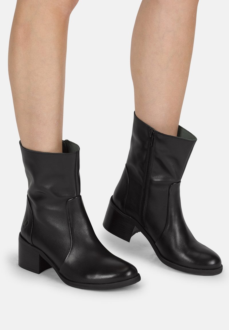 Botas de piel negras hasta el tobillo con punta redonda, tacón bajo y cremallera lateral. Textura suave con un sutil detalle de costura.