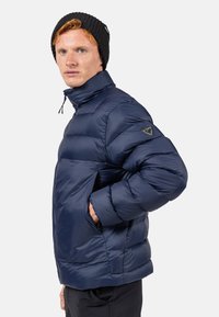Giacca puffer navy con colletto alto, tasche laterali e dettagli con logo sulla manica sinistra. Tessuto liscio e leggero con una texture gonfia.
