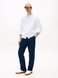 Sweatshirt branco, camisa de colarinho azul claro, calças azul marinho, boné bege, ténis brancos com solas de borracha. Design simples, com pouca marca.
