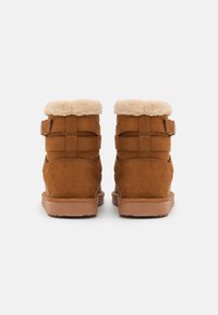 Bruine suède enkelboots met een zachte crèmekleurige bontkraag, dubbele banddetails en een gestructureerde rubberen zool. Achteraanzicht.