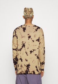 Suéter de punto extragrande en tono arena con diseño de teñido anudado negro. Presenta un cuello redondo y mangas largas. La tela parece suave, con puños y dobladillo acanalados.