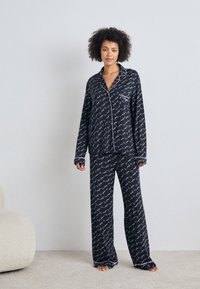 Svart pyjamas-sett med et mønster av hvite linjer, lange ermer og bukser med elastisk linning, detaljert med hvite pipingsrike.