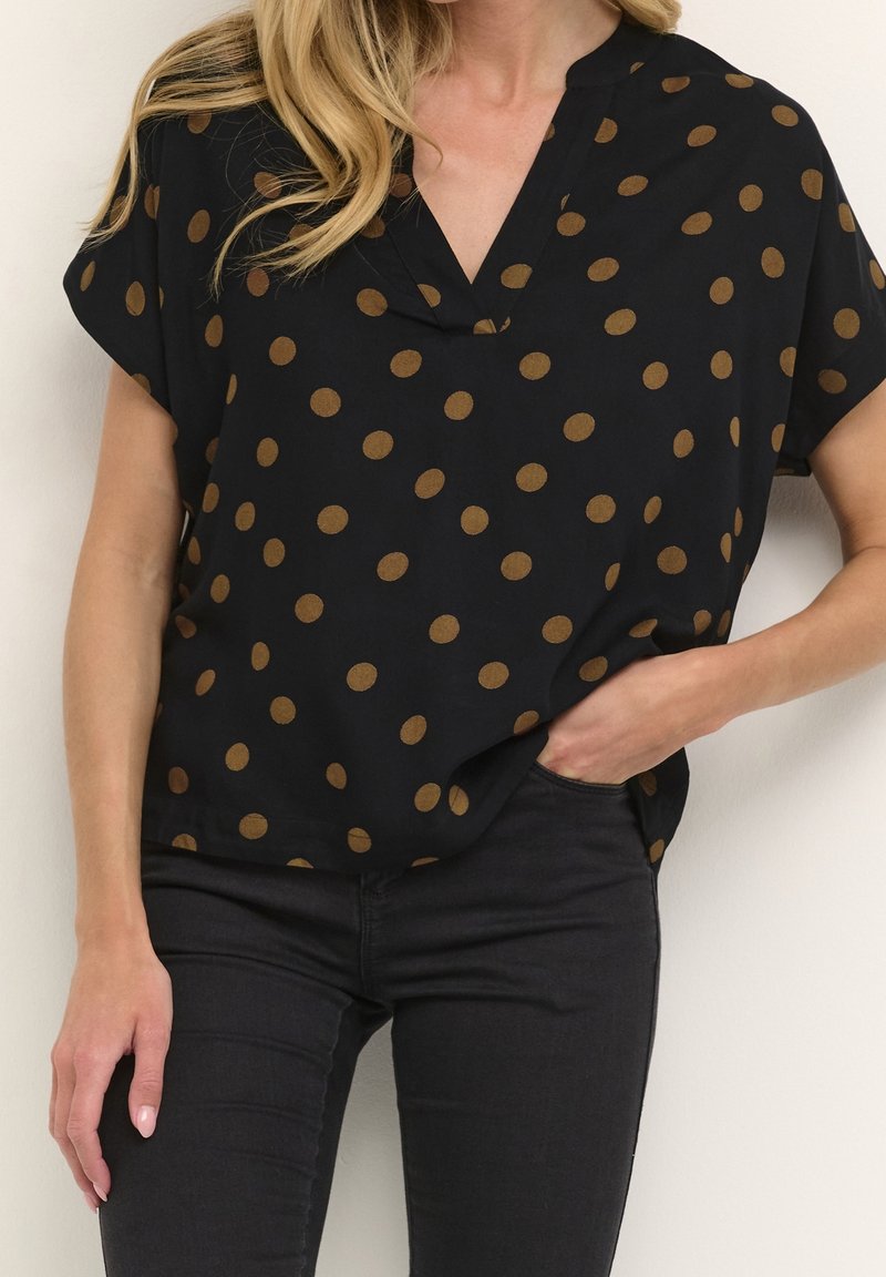 Haut noir à manches courtes avec un col en V et des pois marron, réalisé dans un tissu lisse, accompagné d'un jean foncé.