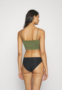 Grön bomullstopp med tunna remmar, matchad med svarta högmidjade bikinitrosor, med en jämn textur och enkel design.