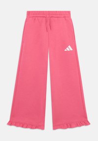 Pantalon de sudation rose avec un design à jambes larges, taille élastique, cordon de serrage et ourlet froncé. Un logo Adidas blanc est situé sur le côté gauche.