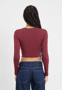 Burgundski dugi rukav uski crop top s rebrastom teksturom, prilagođenog dizajna, okruglog izreza, u kombinaciji s tamnoplavim visokim trapericama.
