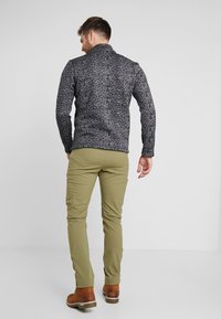 Maglione a maglia a righe in bianco e nero con un alto colletto, abbinato a pantaloni aderenti verde oliva e stivali stringati marroni.