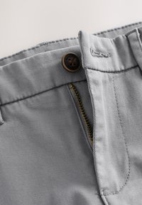 Gros plan sur un pantalon gris clair avec une fermeture éclair en laiton ouverte et un bouton foncé portant la mention « Authentic New York .»