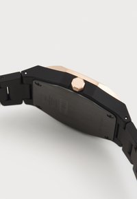 Montre noire avec une couronne hexagonale en or rose et un fond de boîtier noir brossé. Présente un design épuré et moderne ainsi qu'une texture lisse.