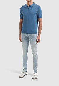 Blauwe kortekleurige poloshirt met een ritskraag, gecombineerd met lichtblauwe slim-fit jeans en witte sneakers met grijze accenten.