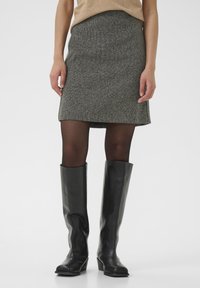 Jupe mini en tweed gris associée à des bottes en cuir noires montantes. La jupe présente une silhouette simple et une finition texturée.