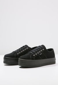 Sneaker platform neri in suede, con punta arrotondata, lacci piatti e suola in gomma testurizzata con elementi di design minimalisti.