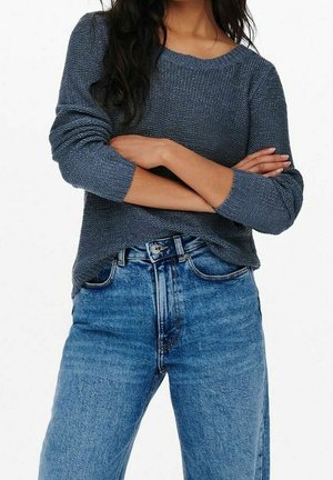 Maglione grigio lavorato a maglia con scollo rotondo e maniche a tre quarti, abbinato a jeans in denim a vita alta di colore blu chiaro.