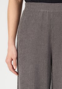 Grå texturerade vida byxor med en rynkad tygfinish. Har hög midja och subtila sid söm detaljer.