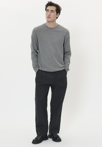 Camisa gris de manga larga combinada con pantalones negros de corte holgado y zapatos negros con cordones. Diseño simple con corte recto y escote redondo.
