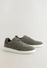 Gray suede sneakers with flat laces, white rubber soles, and black accents. Features stitched detailing and side stripes for added design.