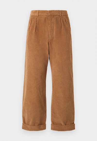 Brune kordfløyelsbukser med vid ben design, med frontfolder og rullede hem. Stoffet har en teksturert, ribbet utseende.