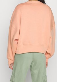 Peskfärgad sweatshirt med sänkt axel, ribbade ärmslut och kort design, som matchas med gröna cargo-byxor med sidofickor.