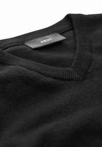 Maglione nero a v collo realizzato in tessuto morbido, con orli a costine. L'etichetta riporta "NEXT". Superficie testurizzata senza pattern o decorazioni.