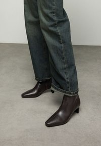 Bottines marron en cuir avec un bout pointu et un petit talon, associées à un jean bleu foncé légèrement ample, retroussé à l'ourlet.